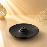 Leela black ceramic Tibetan incense burner with concentric spiral lines and a raised central incense-stick holder.