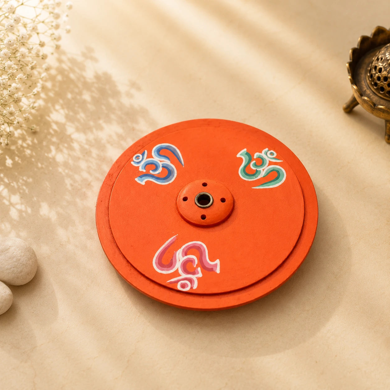 Leela round orange wooden incense burner hand-painted with colourful Om symbols and a central incense holder.